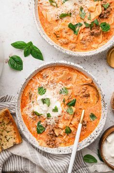 two bowls filled with pasta and cheese on top of a white table next to bread