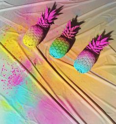 three painted pineapples sitting on top of a white sheet with pink and blue ink