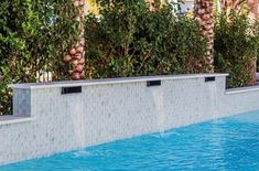 an empty swimming pool surrounded by palm trees and shrubbery with water running down the wall