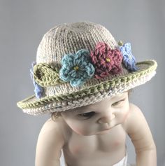 Hand-knit of soft cream-colored cotton yarn with a wide brim to protect little eyes from the sun, this adorable hat is perfect  as an Easter bonnet, for the summer or any time. A garland of flowers encircles the hat, picking up the colored flecks in the yarn, and adding sophisticated style. The palette offers two versions, one with pastel flowers and one with brighter flowers, all in the same tones. The hat comes in 3 sizes, and because it is knit and quite stretchy you may find that it fits lon Cute Beige Wide Brim Hat, Playful Adjustable Cream Hat, Cute Adjustable Cream Bonnet, Cute Knitted Hat For The Beach, Cute Knitted Beach Hats, Adjustable Hand Knitted Mini Hats For Spring, Adjustable Hand-knitted Mini Hats For Spring, Cute Cream Knitted Hats, Cream Handmade Sun Hat With Curved Brim