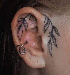 a close up of a person's ear with leaves on it and a spiral design behind the ear