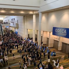 a large group of people standing in an airport lobby with signs on the walls that say deca