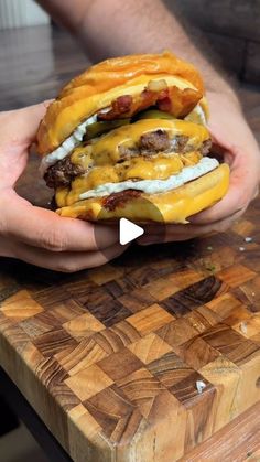 a person holding up a cheeseburger on a cutting board