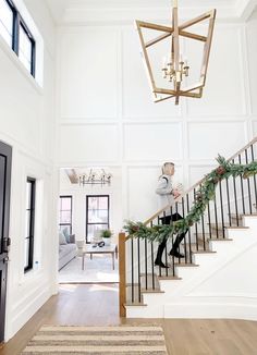 a man is walking down the stairs in a large white house with christmas decorations on it