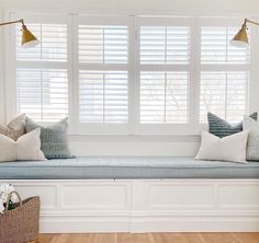 a window seat with several pillows on it in front of two windows, one is white and the other is blue