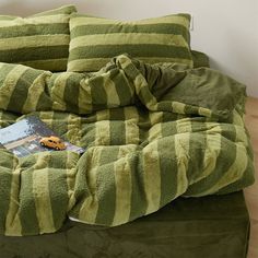 a bed covered in green and white striped blankets with a book on top of it