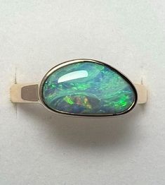 Blue and Green Boulder Opal Ring in 14K Yellow Gold. Australian opal ring in solid 14K yellow gold. Currently Size US 9 1/4 (sizable at check out) 3mm X 1.4mm Solid 14k yellow gold band. Australian Boulder Opal: 2.82 Carats 12.55mm X 7.45mm All of our creations are made out of 14K Gold (Yellow, White, Rose) or 925 Sterling Silver, None are filled or electroplated.  All of our stones are Nature-made, therefore some natural flaws may be present. Hand crafted in the We Work Gems Shop in Washington Boulder Opal Jewelry, Boulder Opal Ring, Australian Opal Ring, Gem Shop, Australian Boulder Opal, Blue Band, Opal Earrings, Opal Ring, Australian Opal