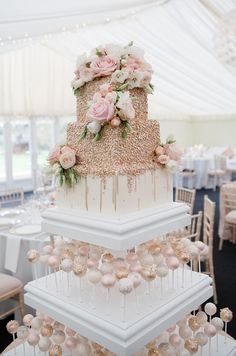 three tiered wedding cake with pink flowers and greenery on top, surrounded by white tablecloths