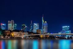 the city skyline is lit up at night with lights reflecting in the water and skyscrapers