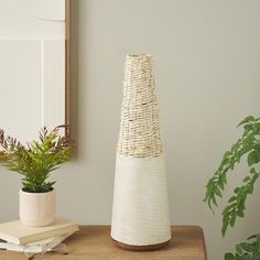 a white vase sitting on top of a wooden table next to a potted plant