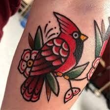 a red bird sitting on top of a branch with leaves and flowers around it's legs