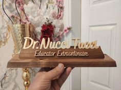 a person holding up a wooden plaque that says dr nuece thau educator extraordnance