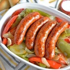 sausages and peppers in a white bowl on a striped towel next to some bread