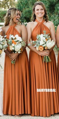 three bridesmaids in orange dresses smile for the camera while holding their bouquets