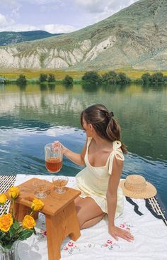 a woman sitting on the edge of a body of water holding a glass of wine