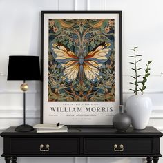 a black table topped with a vase filled with flowers next to a framed butterfly poster