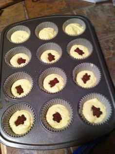 cupcakes with white frosting and chocolate decorations in a muffin tin on a counter