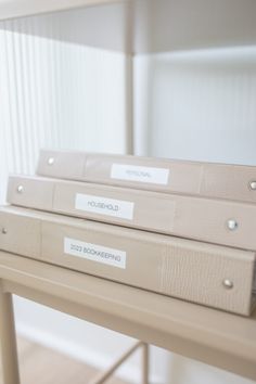 three file folders sitting on top of a wooden table with labels attached to them