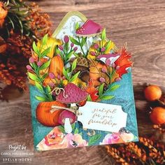 a close up of a card on a table with flowers and pumpkins in the background