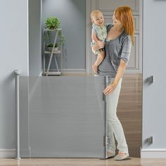 a woman holding a baby in her arms while standing next to a wall mounted mirror