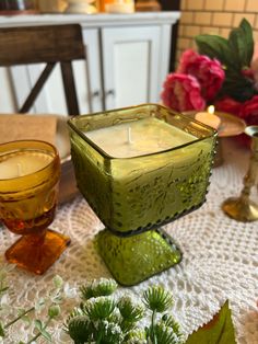 a green candle holder sitting on top of a table next to two glasses and flowers