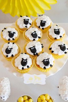 cupcakes with white frosting and black sheep on them are sitting in front of some yellow candies