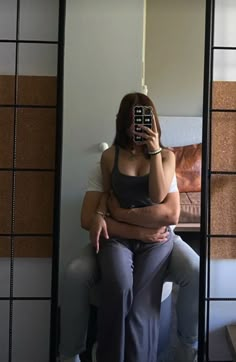 a woman sitting on top of a toilet holding a cell phone to her face while looking at herself in the mirror