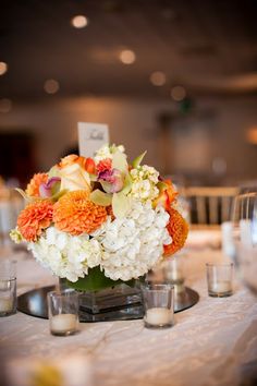 an arrangement of flowers on a table with candles and place cards for guests to sit at