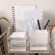 an organized desk with pens, notebooks and other office supplies on a wire rack