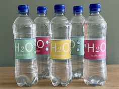 four bottled water bottles sitting on top of a wooden table