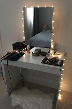 a white desk topped with a mirror and lots of lights next to a night stand