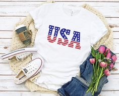 a t - shirt with the american flag on it next to some shoes and flowers