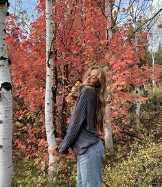 a woman standing in front of some trees with red and yellow leaves on it's branches