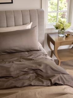 a bed with two pillows on top of it next to a table and chair in front of a window