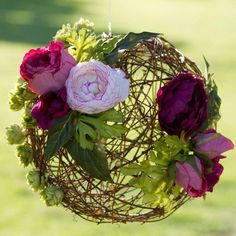 some flowers are hanging from a wire ball in the air with green grass behind it