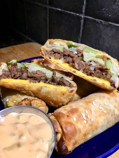 a blue plate topped with three burritos next to a bowl of ranch dressing