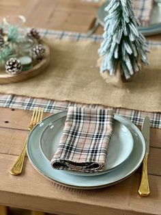 a place setting with plaid napkins and silverware on a table cloth, pine trees in the background