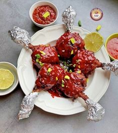 meat wrapped in tin foil on a plate with dipping sauces and lemon wedges