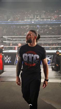 a man walking in the middle of a wrestling ring wearing a black t - shirt