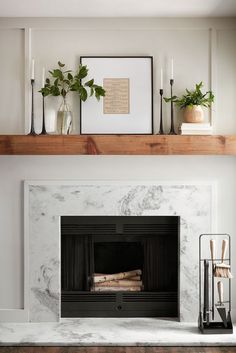 a fireplace with white marble surround and shelves above it, surrounded by candles and plants