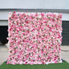 pink and white flowers are arranged on the side of a large flowered wall in front of a garage