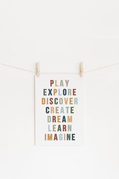 a white wall with some clothes pins hanging from it's sides and the words play explore create dream learn imagine