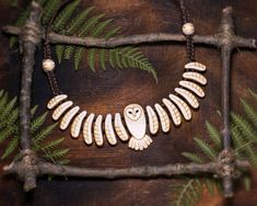 an owl necklace is displayed on a branch with fern leaves and other branches around it