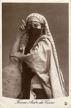 an old photo of a woman with a veil on her head holding a large jug