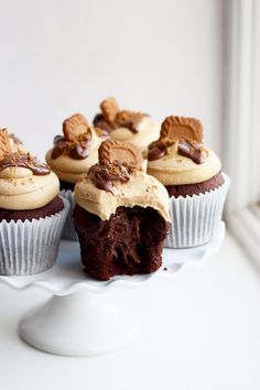 chocolate cupcakes with peanut butter frosting and teddy bears on top sitting on a white cake plate