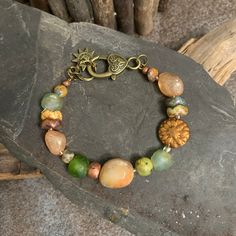 "Summertime" - The bracelet features peach silver coated quartz gemstone that glimmer like the hot sky of a late summer afternoon.  The deep greens of African glass and agate rounds are reminiscent of the thick park grass with the wavey floral discs being the prolific perennial summer flowers with the rust colored Dahlia coin as the grand centerpiecre of the gardens. A large jade nugget pulls the landscape together.  A beautiful bronze heart lobster claw closure completes the summertime cirlce.  As Ella Fitzgerald sings while Louis Armstrong trumpets, "Summertime, and the living is easy". Grab a pcinic basket, a blanket and a good book and look will be complete. Size 7.50. I can adjust this to fit up to to 8.5 inches.  Please let me know your desired size. I begin each piece by hand select Bohemian Orange Agate Jewelry, Bohemian Amber Beaded Bracelets Hand-strung, Orange Bohemian Bracelets For Festivals, Bohemian Orange Bracelets For Festivals, Orange Bohemian Beaded Bracelets, Bohemian Orange Hand-strung Bracelets, Bohemian Orange Hand-strung Bracelet, Orange Gemstone Beads Jewelry For Beach, Handmade Orange Agate Beaded Bracelets