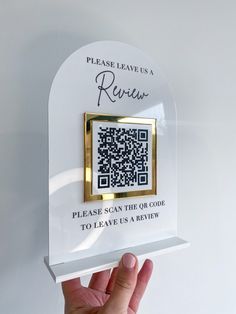 a person holding up a qr - code plaque in front of a white wall