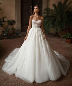 a woman in a white wedding dress standing on a brick floor next to a plant