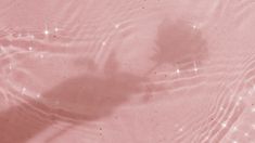 the shadow of a person's hand in shallow water on a pink sand beach