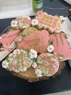 some decorated cookies on top of a wooden stump with flowers and words written in pink